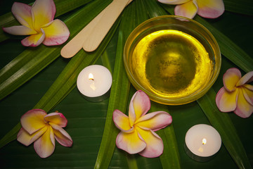 Sugaring Hair Removal Set with Sugar Paste and Spatula on Beautiful Background with Frangipani Flowers and Palm Tree Leaves with Candles in Spa Salon