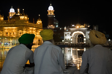 Fototapeta na wymiar Three sikhs sitting at night in the Golden Temple, the most important temple and pilgrimage site of Sikhism, located in Amritsar, India.
