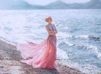 lovely slender girl in a light pink dress is walking along the sandy shore of the beautiful blue...
