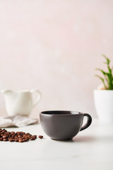 Espresso in a matte black ceramic coffee cup with roasted coffee beans. Feminine rose background with copy space. High resolution image.