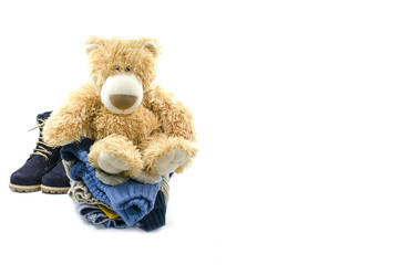 Soft toy sits on a pale of clothes on a white background