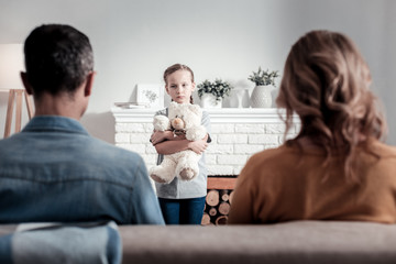 Upset lonely girl looking at the parents while standing in front of them