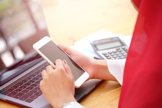 Attractive young Asian wearing red hijab  using her mobile smartphone at workspace desk.