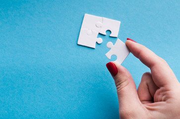 Hand putting last piece of puzzle on blue background