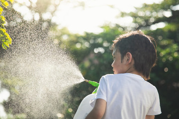 Cute Asian child watering tree with spraying fertilizer in the garden