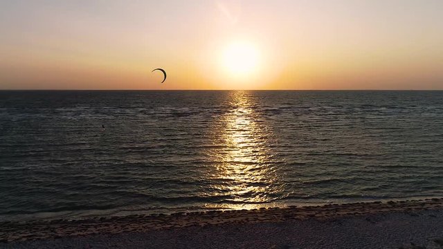 Dron slowly descends to the beach, sea view where a lone person engages in kitesurfing