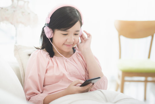 Beautiful Asian girl listening to music  sitting on a sofa in the living room at home