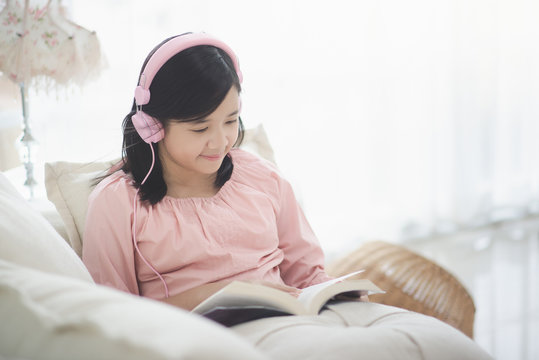 Beautiful Asian girl resting on Sofa at the Living Room While Reading a book