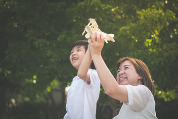 Cute Asian mother and son playing wooden airplane together in the park outdoors