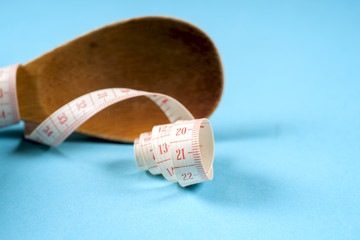 Wooden spoon with a measuring tape on a blue background, diet, healthy lifestyle.