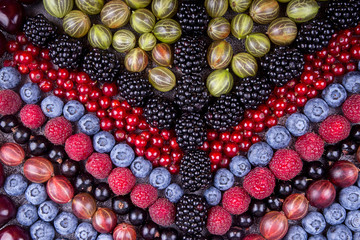  Geometric pattern of summer fruits and berries: gooseberries, raspberry, red and black currant, blueberry, blackberries,  sweet cherry over on grey concrete background.