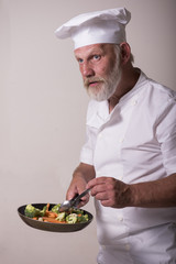 Vertical image of a mature chef cooking a stir-fry on a white background 