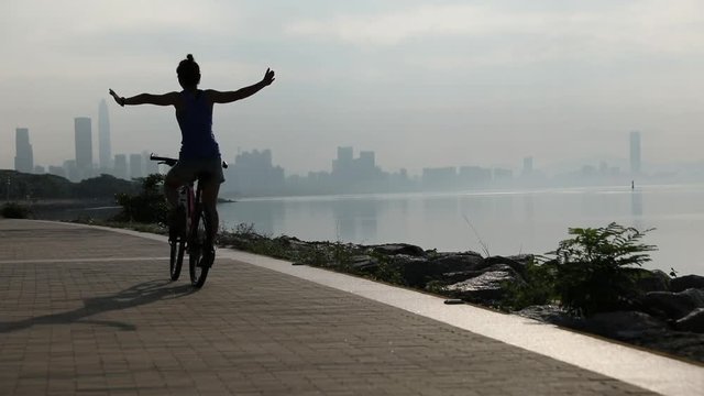Slow motion woman Riding Bike on Seaside Road At Sunrise With Hands Up In Air