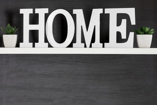 Home letters decor on white shelf with dark wood background, copy space