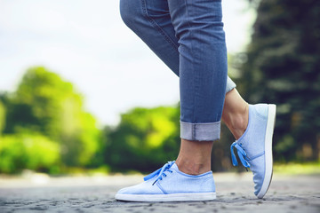 legs of a girl in jeans and blue sneakers on a sidewalk tile, a young woman strolling in a summer...