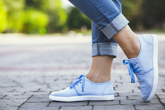 legs of a girl in jeans and blue sneakers on a sidewalk tile, a young woman strolling in a summer park