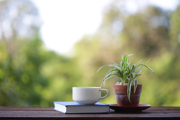 White coffee cup with notebook on wooden table with green plants