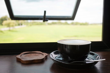 Black coffee cup with cappuccino on wooden table with glass window in a beautiful morning.