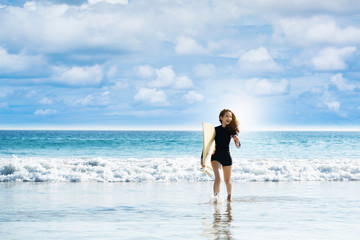 Girl holding surfboard running down to sea. Bright blue sea in the evening for surfing. During long weekend of summer Feel refreshed and relaxed. sunscreen help protect the skin against sun exposure.