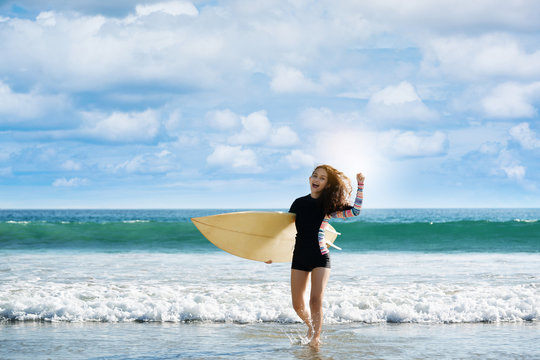 Girl holding surfboard running down to sea. Bright blue sea in the evening for surfing. During long weekend of summer Feel refreshed and relaxed. sunscreen help protect the skin against sun exposure.