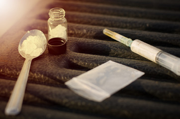 Drug syringe and cooked heroin laying across a spilled bag of heroin on black table