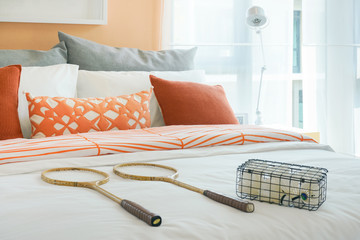 Rackets and box of shuttlecocks on bed in orange color scheme bedding style at home