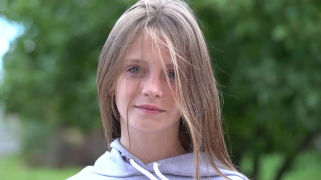 Beautiful blond young girl with freckles outdoors looking, hair blowing in wind on nature background, close up portrait, slow motion
