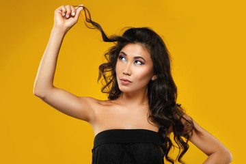 Asian woman with a beautiful curly hair and make-up on yellow background - obrazy, fototapety, plakaty