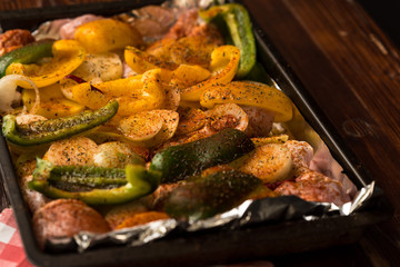 baking sheet, in the middle are vegetables, peppers, onions, potatoes and pieces of white meat sprinkled with spices and prepared for baking