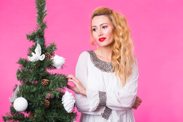 Christmas and people concept - young blonde woman thinking about next year near the christmas tree over the pink background