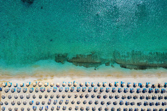 Aufgereihte Sonnenschirme und Sonnenliegen am Strand von Kalafatis auf Mykonos, Griechenland