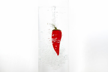 Red chilli pepper drops into clear clear water. There are a lot of bubbles in the water. White background, close-up