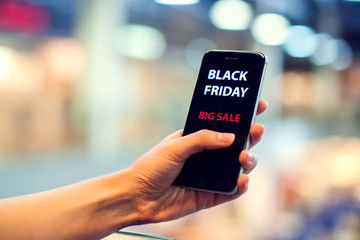 People, sale, consumerism, advertisement concept - close up of woman's hand holding shopping bags and smartphone with black friday inscription