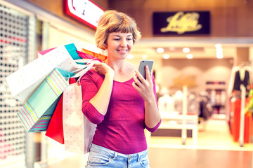 Female customer with cellular phone and shopping bags in the mall