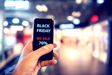 People, sale, consumerism, advertisement concept - close up of man's hand holding shopping bags and smartphone with black friday inscription