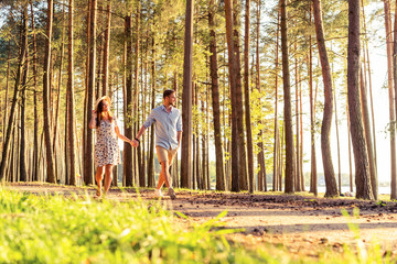 Fototapeta premium Young couple in love walking in the autumn park holding hands looking in the sunset.