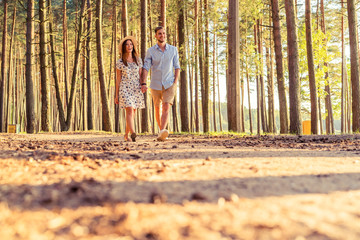 Young couple in love walking in the autumn park holding hands looking in the sunset.