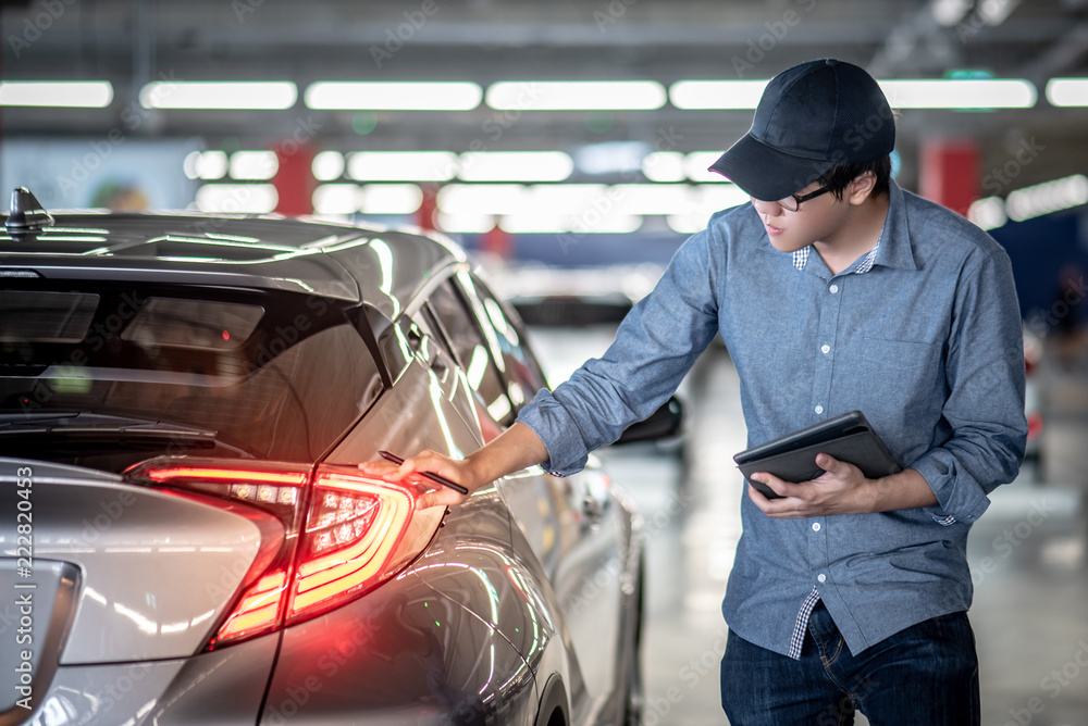 Wall mural asian auto mechanic holding digital tablet checking tail light in auto service garage. mechanical ma