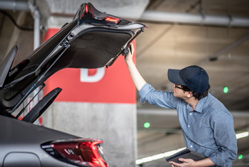 Fototapeta na wymiar Young Asian auto mechanic holding digital tablet checking tailgate in auto service garage. Mechanical maintenance engineer working in automotive industry. Automobile servicing and repair concept