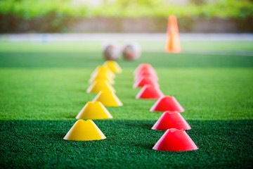 Cone marker and football are soccer training equipment on green artificial turf.