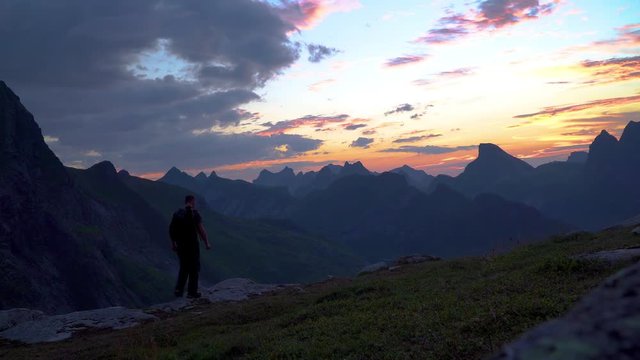 A woman and a man with a backpack travel in the mountains and enjoys the early dawn. Beautiful view of the mountain tops on the Lofoten Islands. Norway 4K