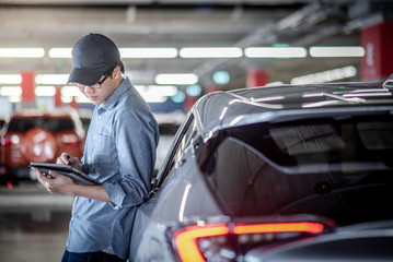 Young Asian auto mechanic holding digital tablet checking the car in auto service garage. Mechanical maintenance engineer working in automotive industry. Automobile servicing and repair concept
