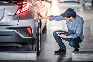 Young Asian auto mechanic holding digital tablet checking car wheel in auto service garage....