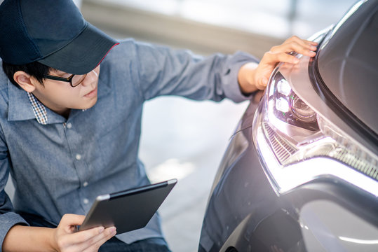 Young Asian auto mechanic holding digital tablet checking headlight in auto service garage. Mechanical maintenance engineer working in automotive industry. Automobile servicing and repair concept
