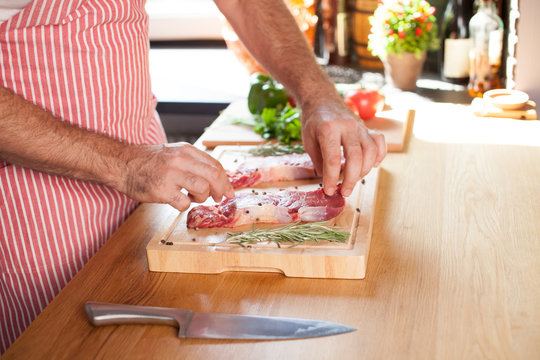 Raw beef tenderloin steak on a cutting board with rosemary pepper salt fork and cutter.