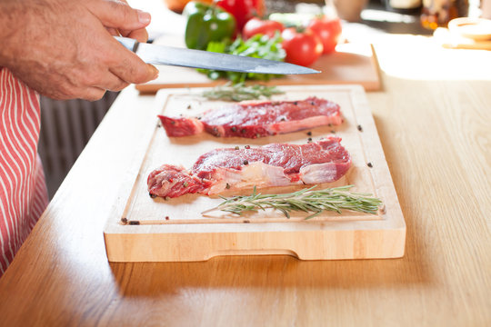 Raw beef tenderloin steak on a cutting board with rosemary pepper salt fork and cutter.