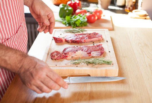 Raw beef tenderloin steak on a cutting board with rosemary pepper salt fork and cutter.