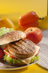 Chicken burger with bell pepper and lettuce with cherry red and yellow tomato on yellow background 