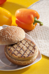 Chicken burger with bell pepper and lettuce with cherry red and yellow tomato on yellow background 