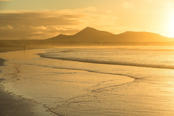 Fototapeta na wymiar Golden sunset in pastel colors over the ocean strip of low tide with volcanoes on the horizon